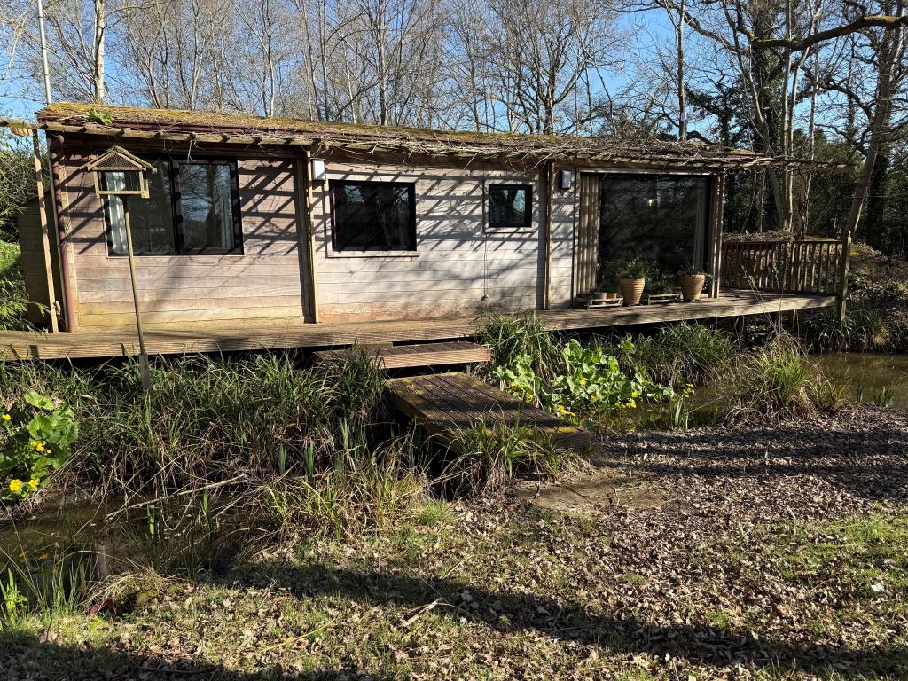 Lot: 80 - FISHING LODGE AND LAKE ON APPROX. ONE ACRE - Front view of wooden lodge from island